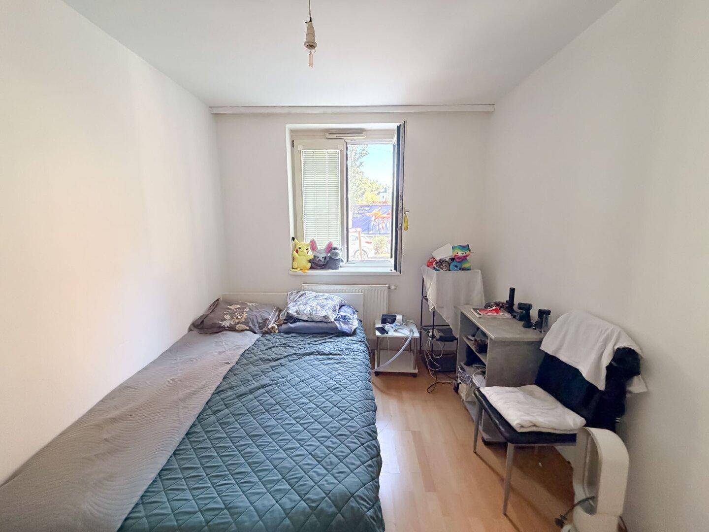 Helles Schlafzimmer mit Einzelbett, Fenster und Holzboden, einfach eingerichtet.