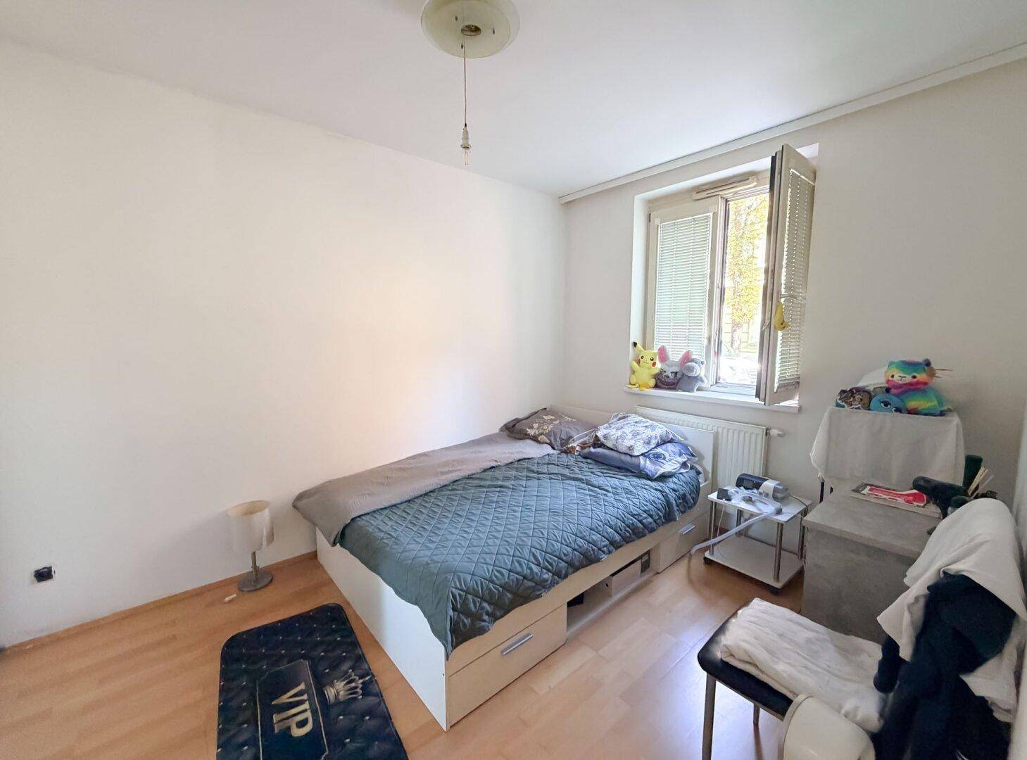 Einfaches Schlafzimmer mit Einzelbett, Fenster und Holzboden, ideal als Kinder- oder Gästezimmer.