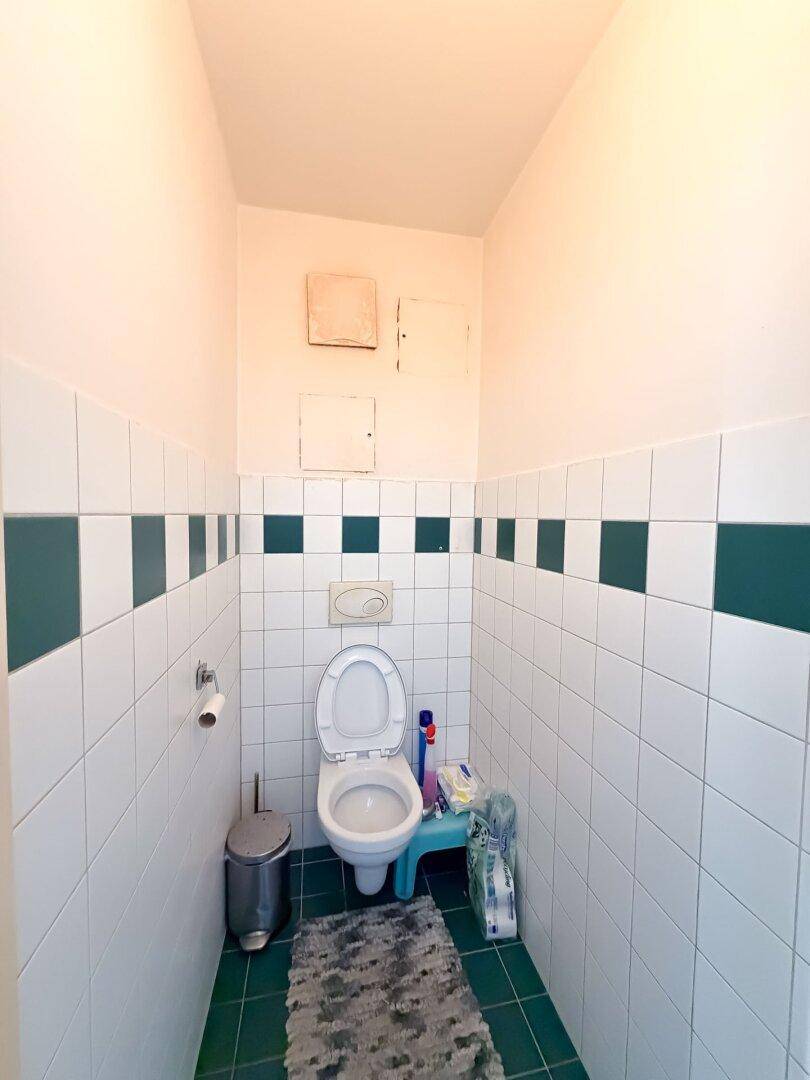 Separates WC mit Wand-WC und weiß-grünen Fliesen an den Wänden.