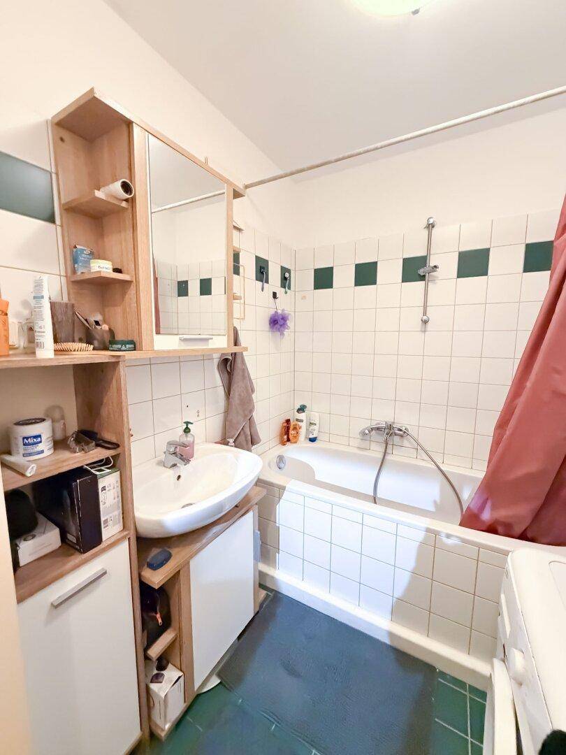 Badezimmer mit Badewanne, Waschbecken und Spiegelschrank, gefliest in Weiß und Grün.