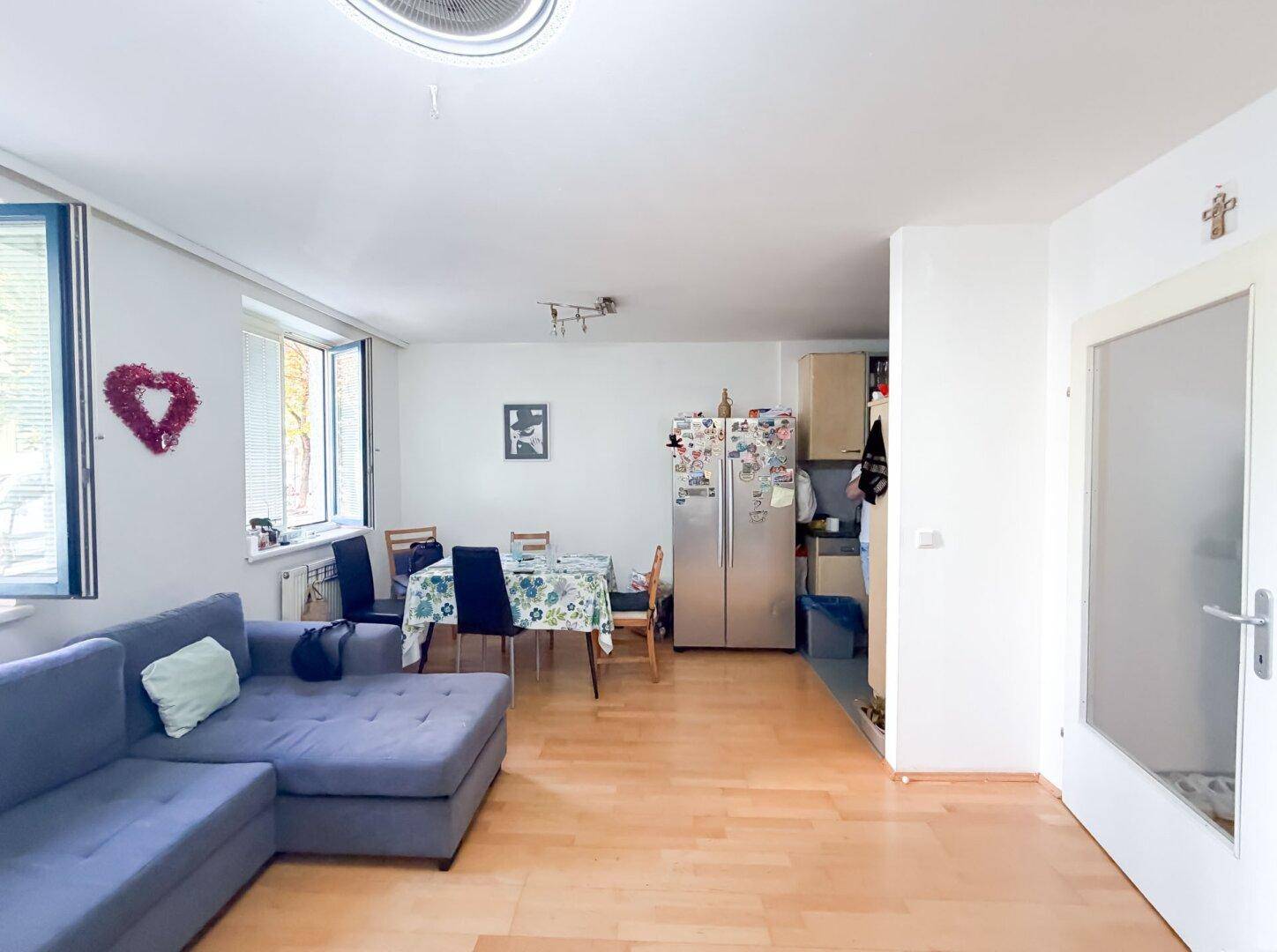 Heller Wohn- und Essbereich mit Holzboden, großem Kühlschrank und Zugang zu einem weiteren Raum.