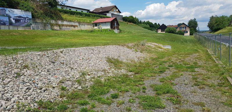 Große Schotterfläche und Rasen mit einem Steinhaufen, angrenzend an eine Straße und weitere Gebäude.