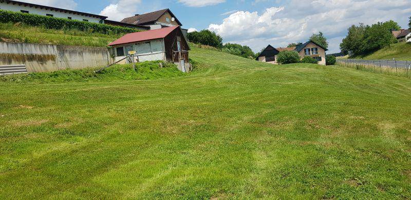 Gepflegte Rasenfläche mit leichtem Hang, umgeben von ländlicher Bebauung und grüner Natur.