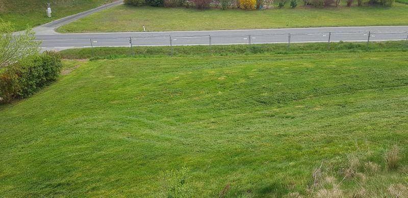 Weitläufige, grüne Rasenfläche mit Blick auf eine Straße und die hügelige Landschaft im Hintergrund.