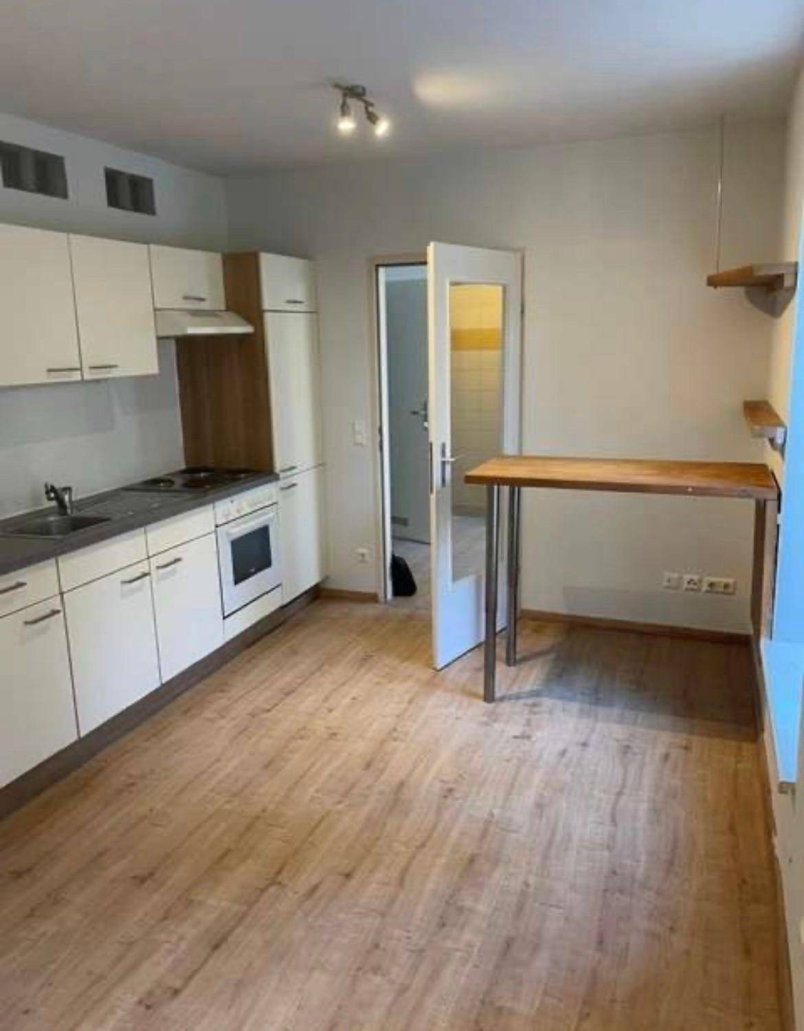 Helle Küche mit Laminatboden, weißen Einbauschränken und einer Frühstückstheke.