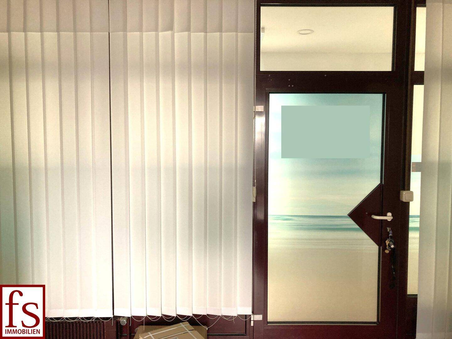 Innenansicht einer Tür und eines Fensters mit vertikalen Jalousien, die das Tageslicht filtern.