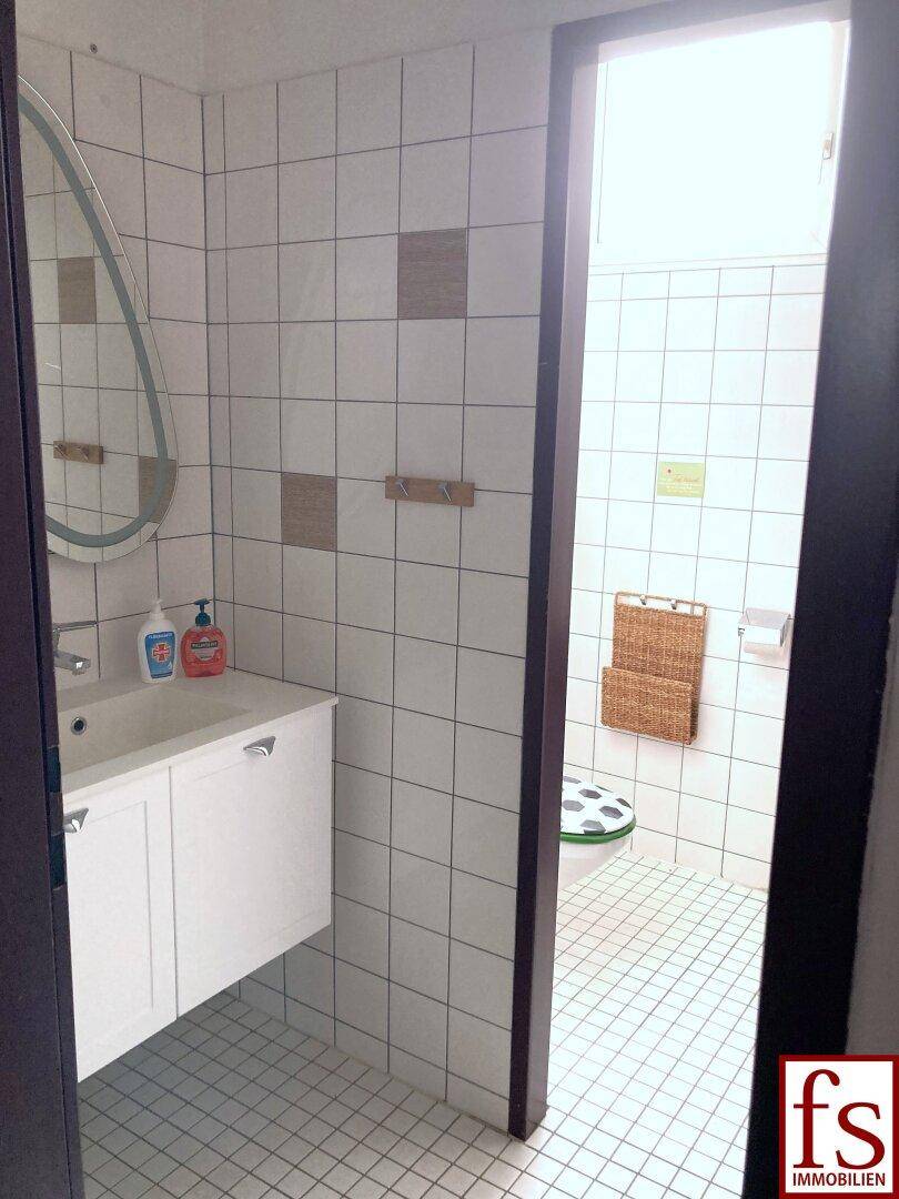Gefliestes Badezimmer mit Waschbecken, Spiegel und Toilette in hellem, funktionalem Design.
