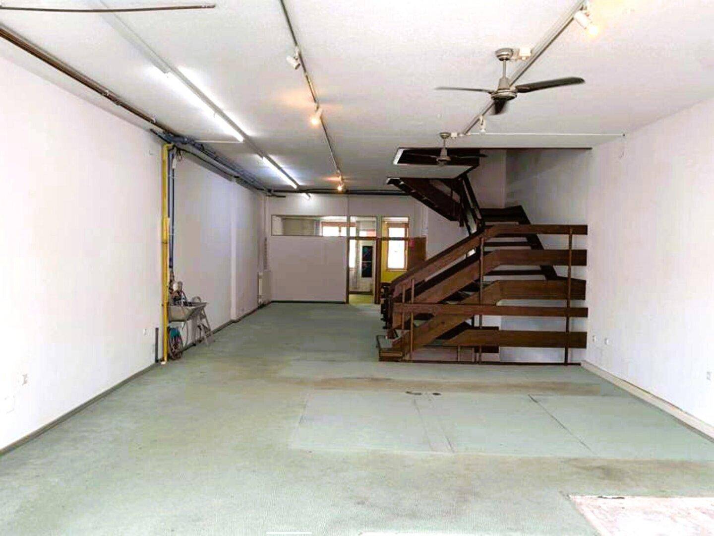 Weitläufiger Innenraum mit Holztreppe, grünem Teppich und sichtbaren Leitungen an der Decke.
