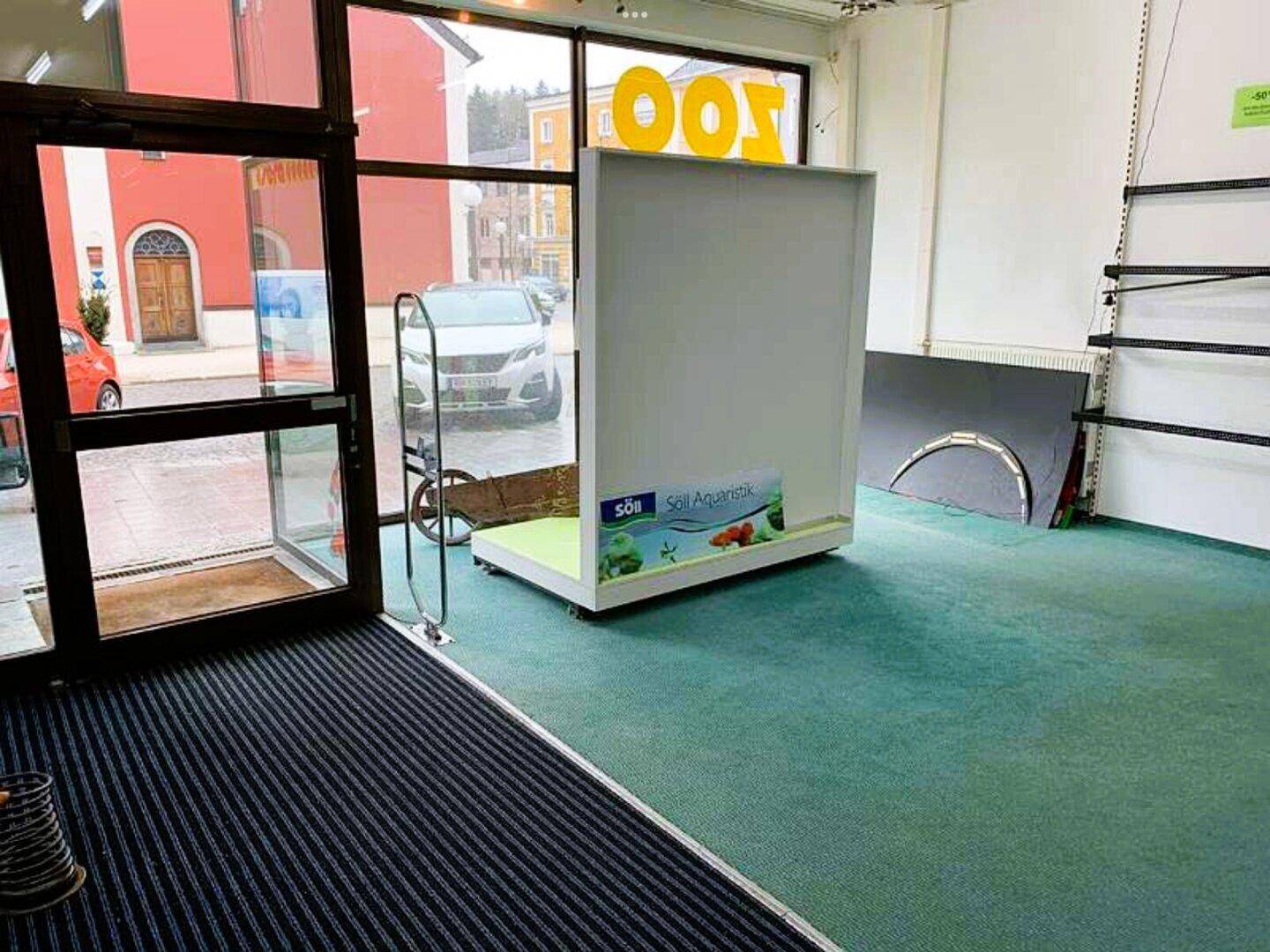 Innenansicht eines Ladenlokals mit grünem Teppichboden und großen Schaufenstern.