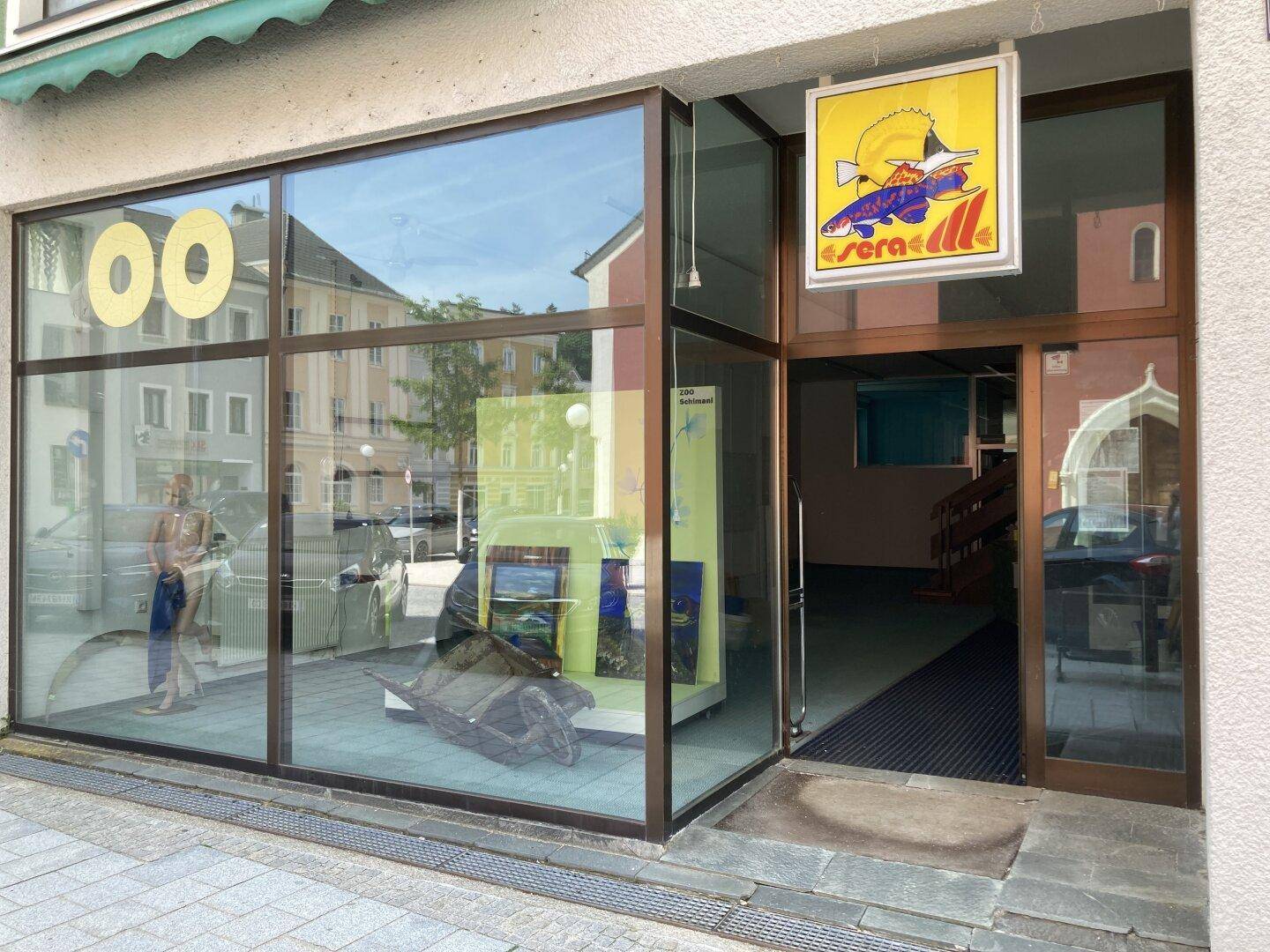 Eingangsbereich eines Geschäfts mit großen Glasfenstern und einer Werbetafel.