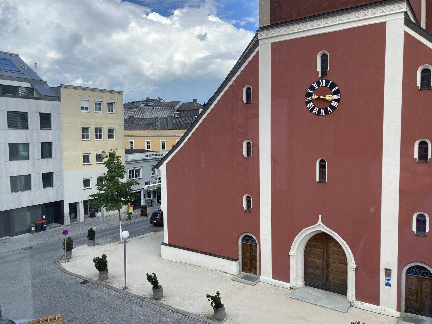 Blick aus einem Fenster auf eine rote Kirche mit Uhr und umliegende Stadtgebäude.