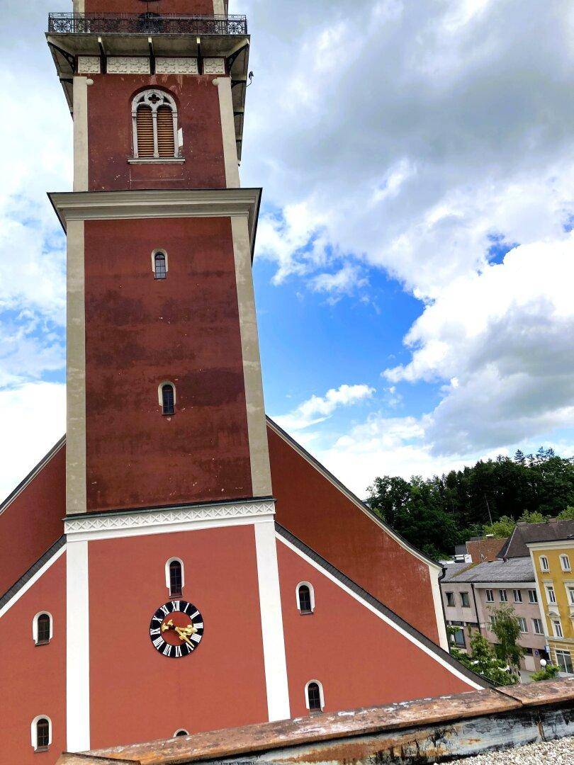 Detailansicht des roten Kirchturms mit Uhr und historischer Architektur unter bewölktem Himmel.
