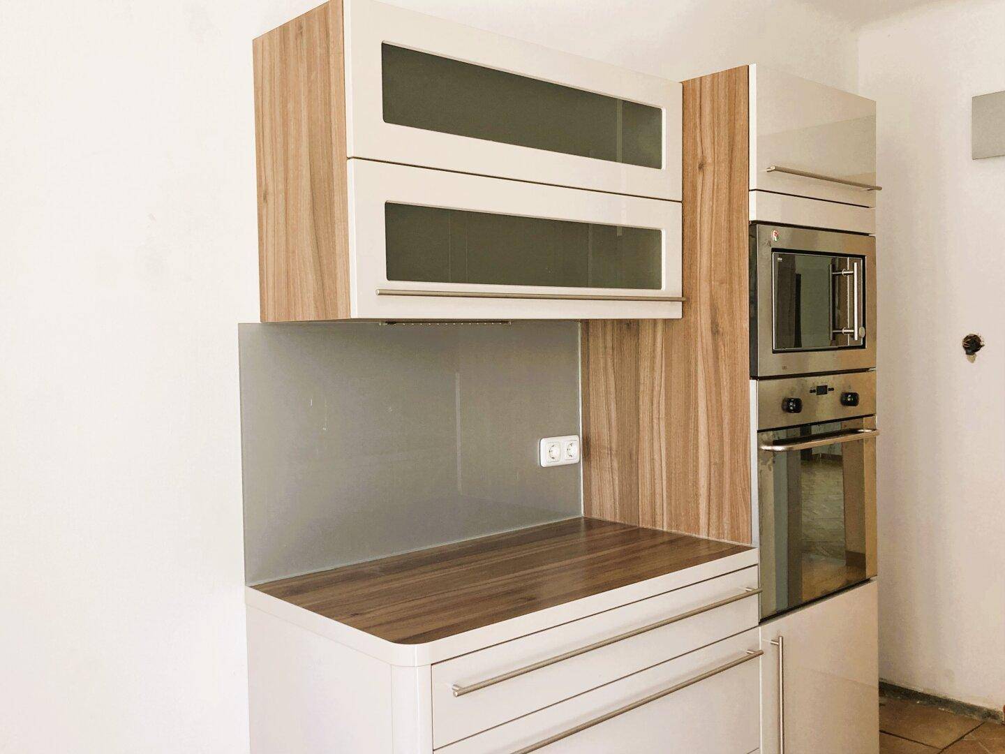 Moderne Küchenzeile mit beigen Hochglanzschränken, Holzdekor und integrierten Geräten.