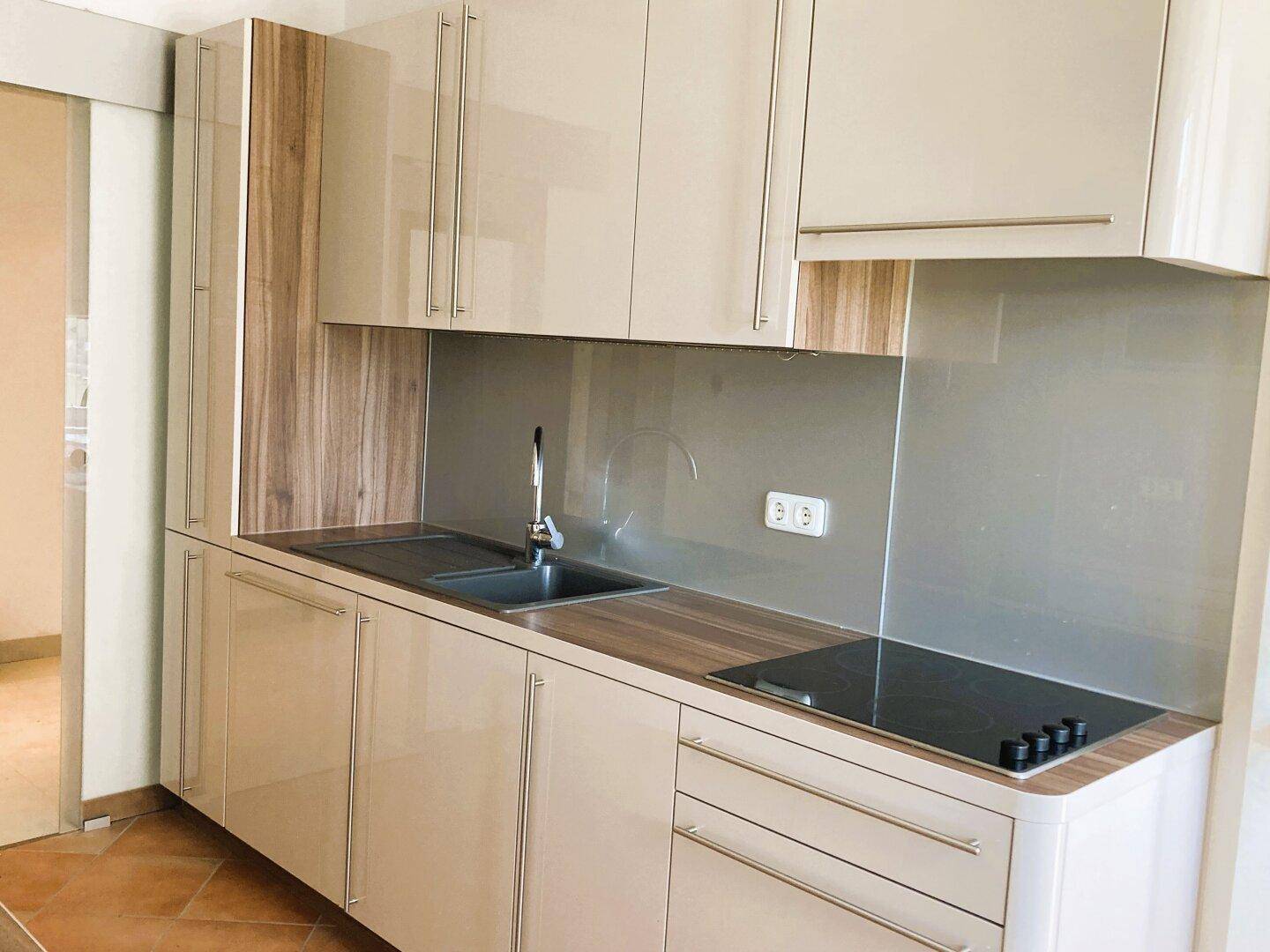 Moderne Küche mit beigen Hochglanzfronten, Holzarbeitsplatte und Induktionskochfeld.