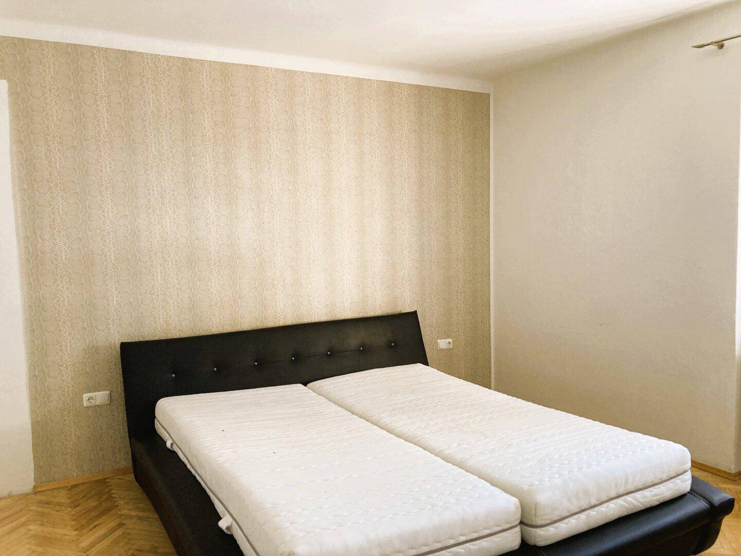 Schlafzimmer mit Doppelbett und gemusterter Tapete, bereit zur individuellen Gestaltung.