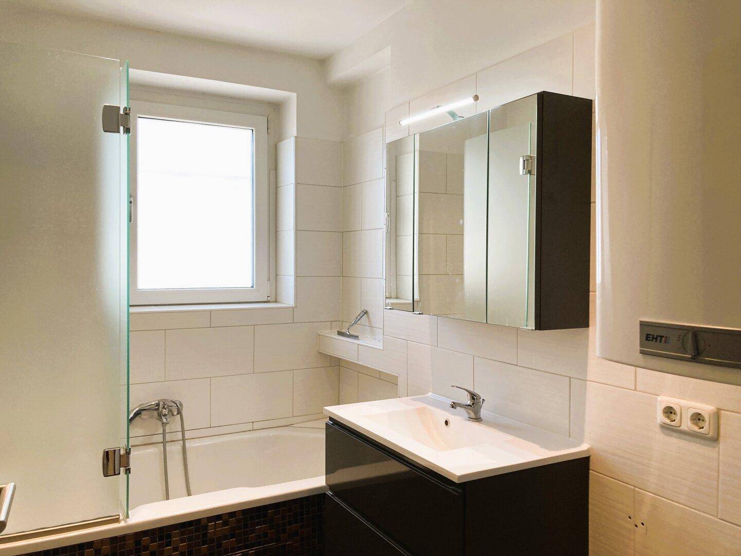 Modernes Badezimmer mit Badewanne, Duschabtrennung, Fenster und Waschtischunterschrank.