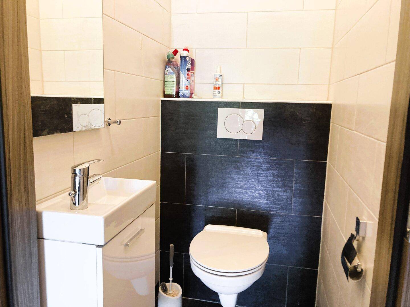 Kleines Gäste-WC mit Wand-WC, Handwaschbecken und modernen Fliesen in Schwarz-Weiß.