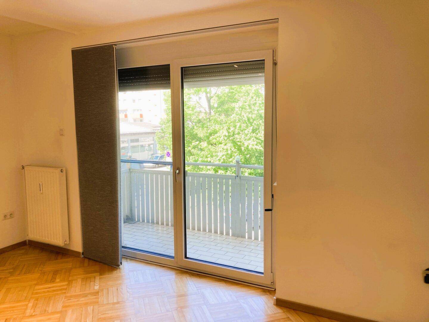 Heller Wohnbereich mit großem Fenster und Balkontür, die einen Blick ins Grüne bietet.