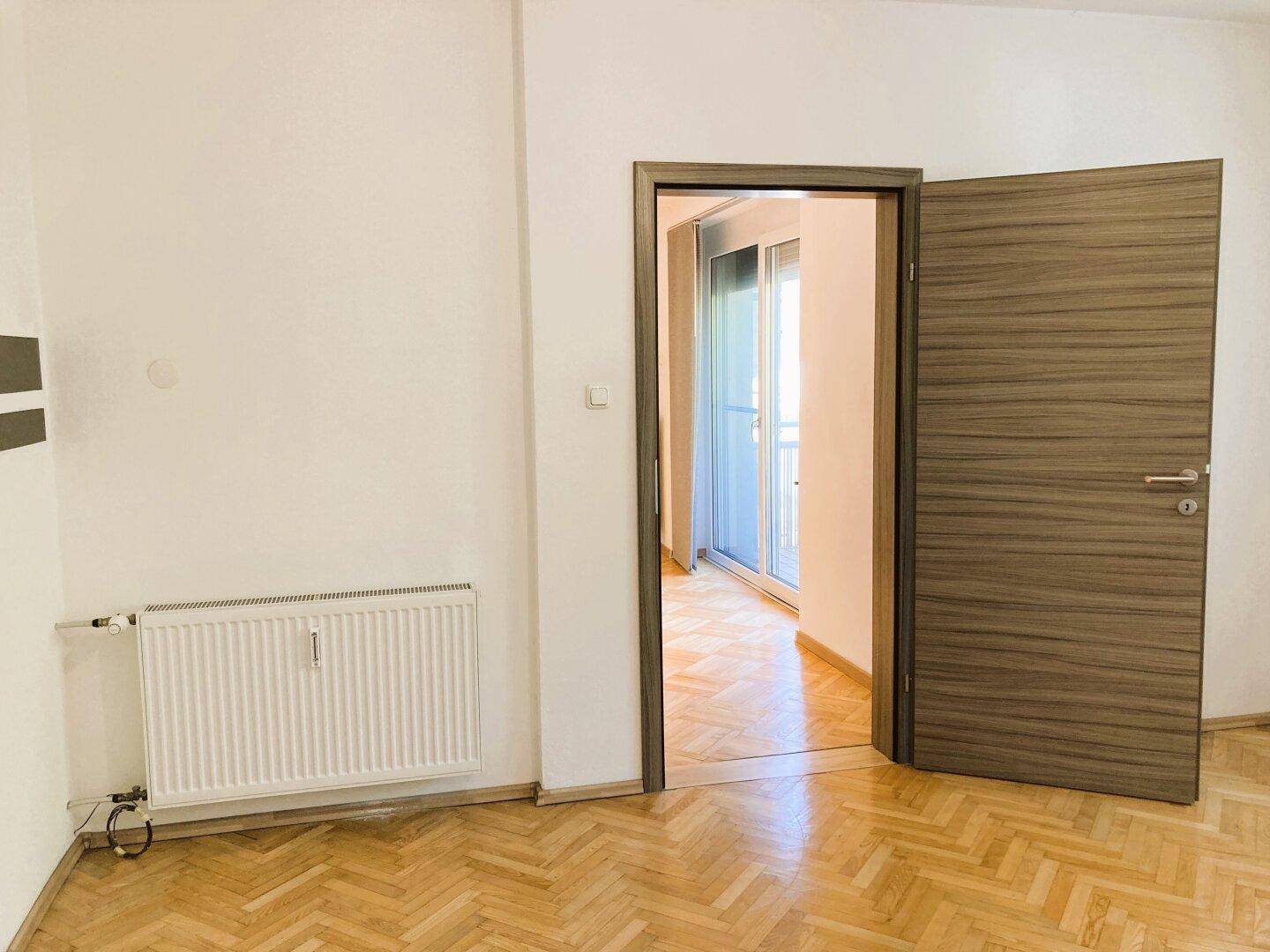 Schlafzimmer mit Parkettboden und Zugang zu einem weiteren Raum mit Balkon.