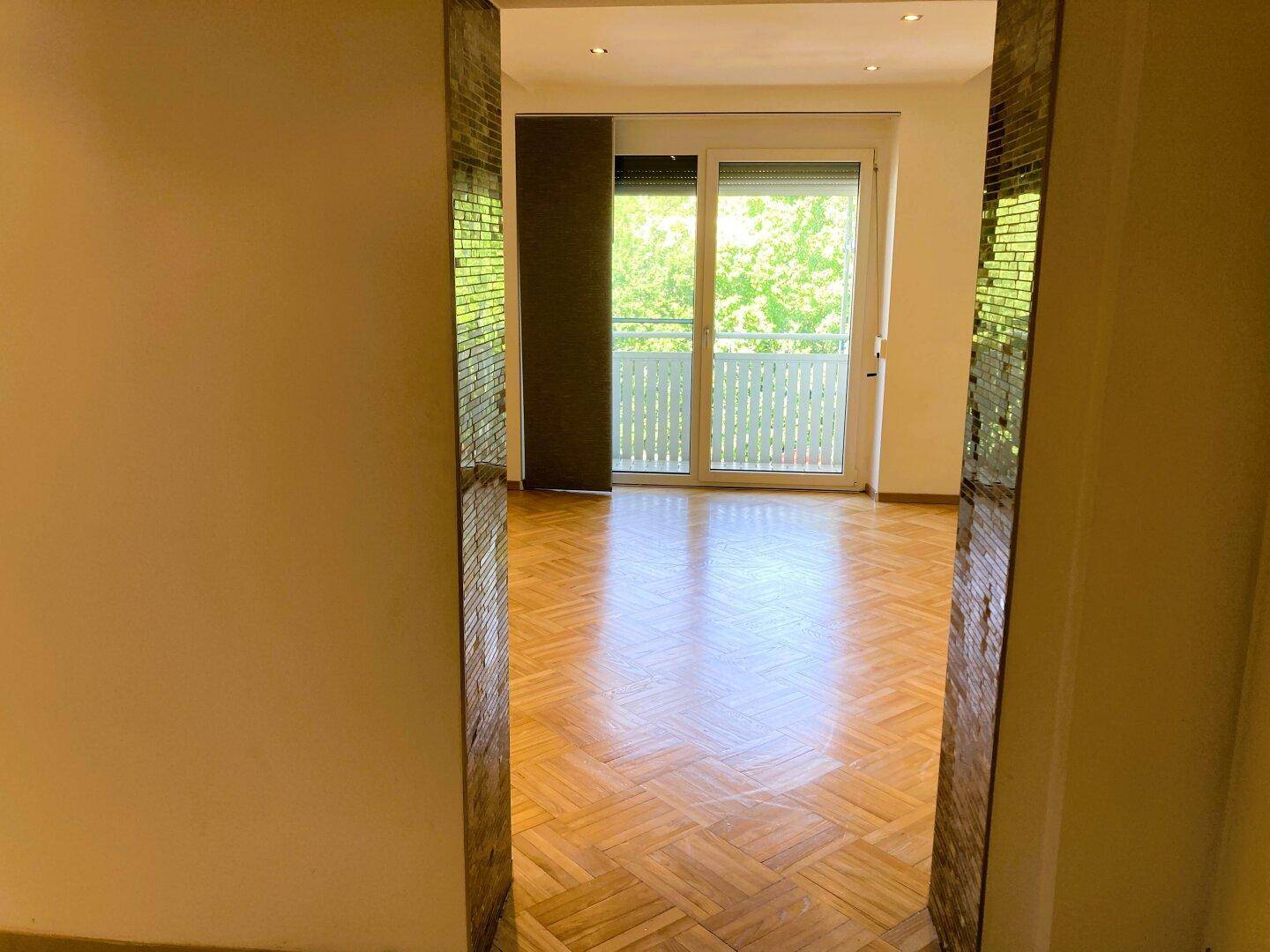 Geräumiges Wohnzimmer mit Fischgrätparkett und direktem Zugang zum sonnigen Balkon.