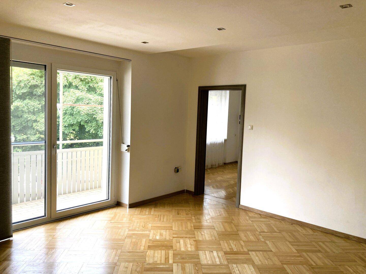 Geräumiges Wohnzimmer mit Fischgrätparkett und direktem Zugang zum sonnigen Balkon.