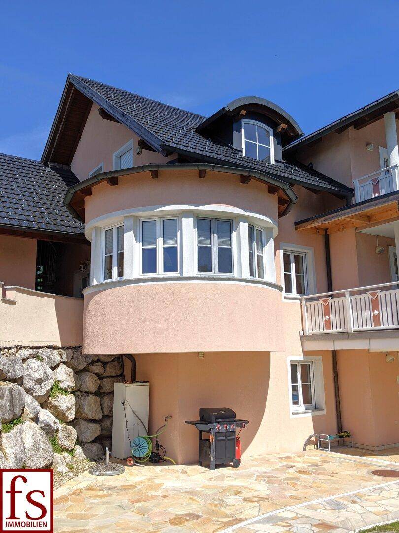 Seitenansicht des Hauses mit markantem Erkerfenster und Grillbereich auf der gepflasterten Fläche.