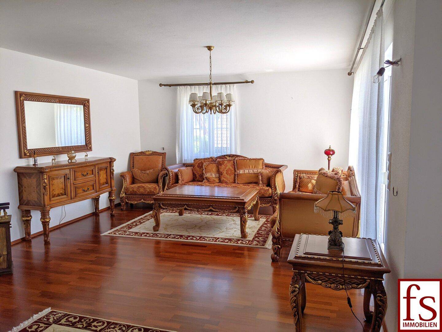Elegantes Wohnzimmer mit dunklem Parkettboden, klassischen Möbeln und großen Fenstern für viel Tageslicht.