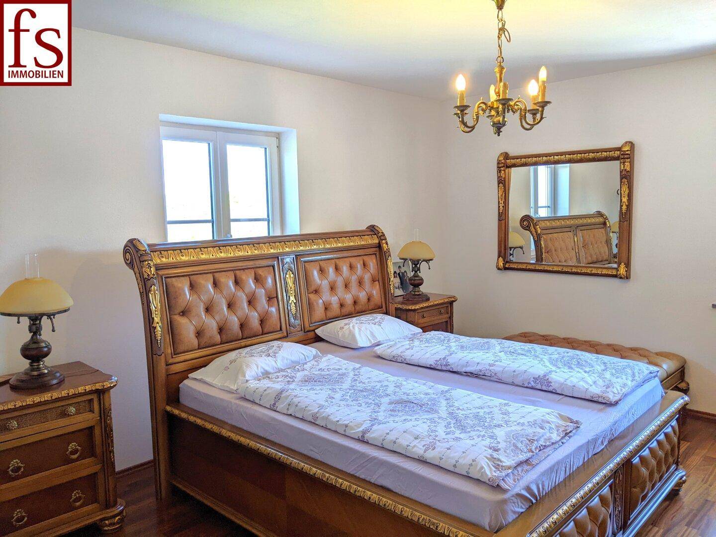 Schlafzimmer mit opulentem Holzbett, passenden Nachttischen und einem klassischen Kronleuchter.