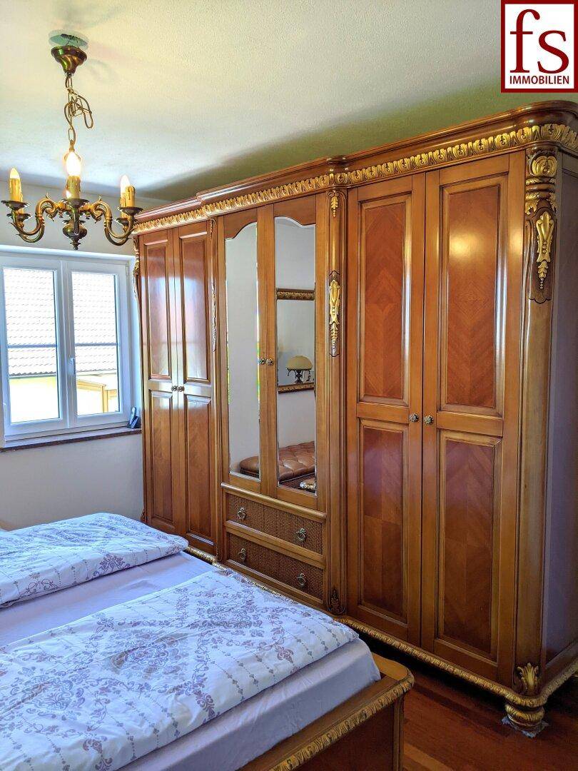 Geräumiges Schlafzimmer mit großem, verziertem Holzschrank und Fenster für Tageslicht.