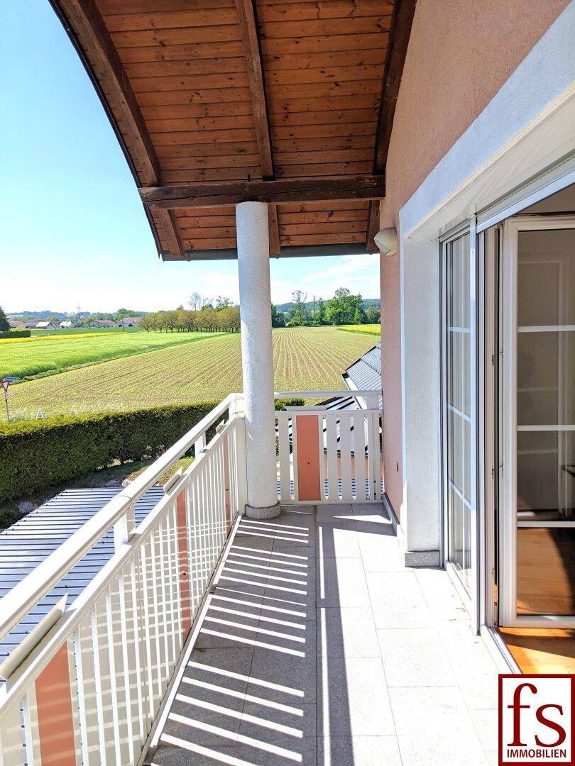Sonniger Balkon mit weitem Blick über die grüne Landschaft und Felder.