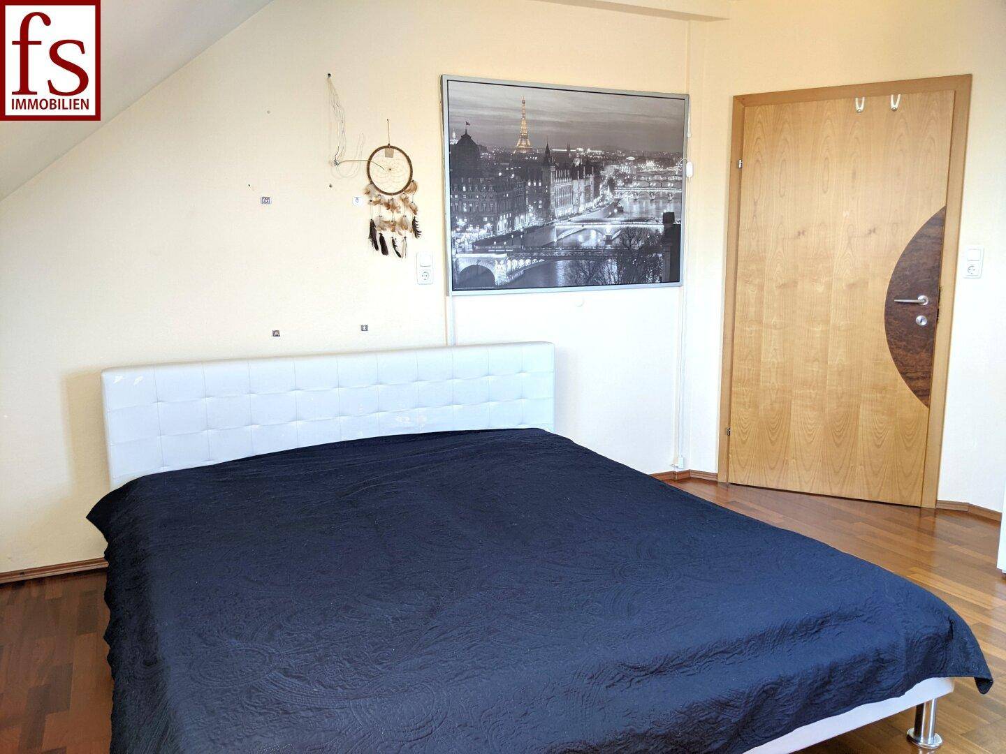 Schlafzimmer im Dachgeschoss mit modernem Bett und Holztür, unter einer Dachschräge.