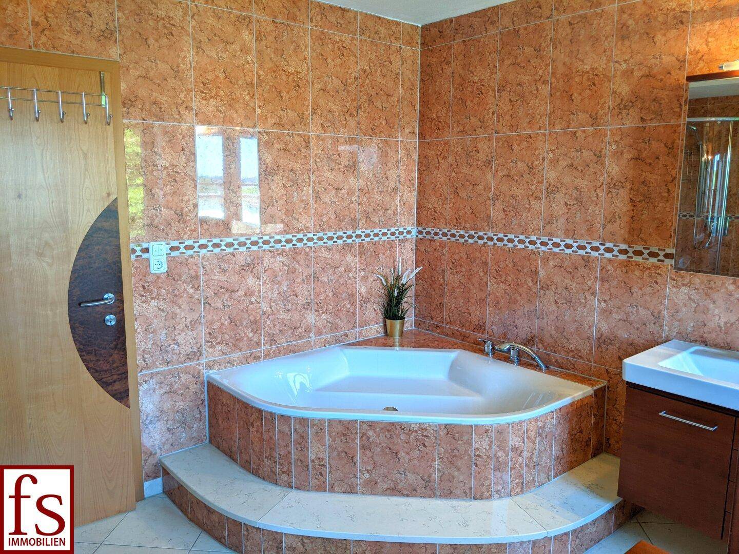 Badezimmer mit Eckbadewanne und gemusterten Fliesen in warmen Brauntönen.