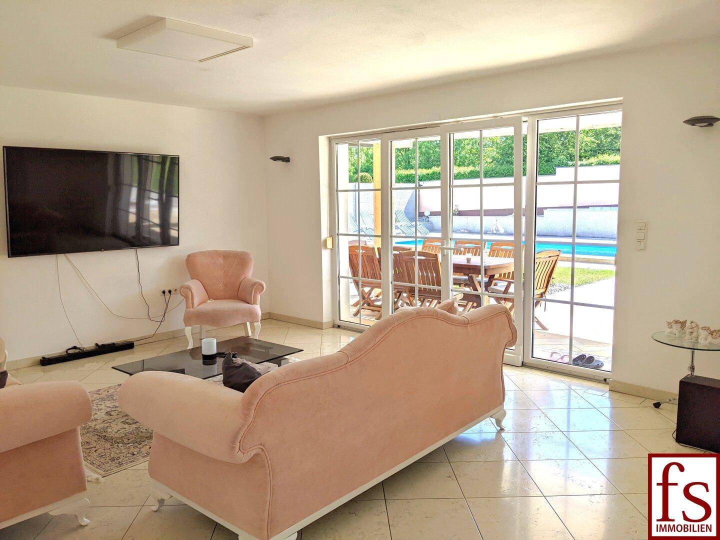Helles Wohnzimmer mit Fliesenboden und großen Schiebetüren mit Blick auf den Poolbereich.