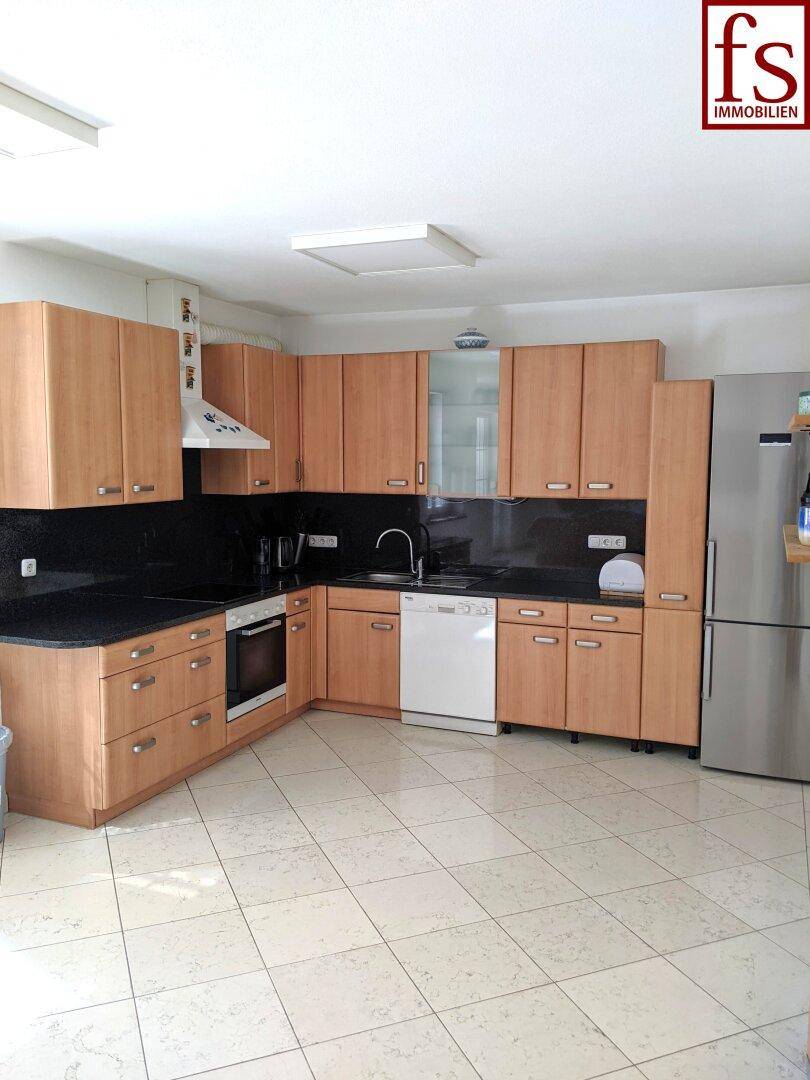 Geräumige Küche mit hellen Holzschränken, dunklen Arbeitsplatten und modernen Geräten.
