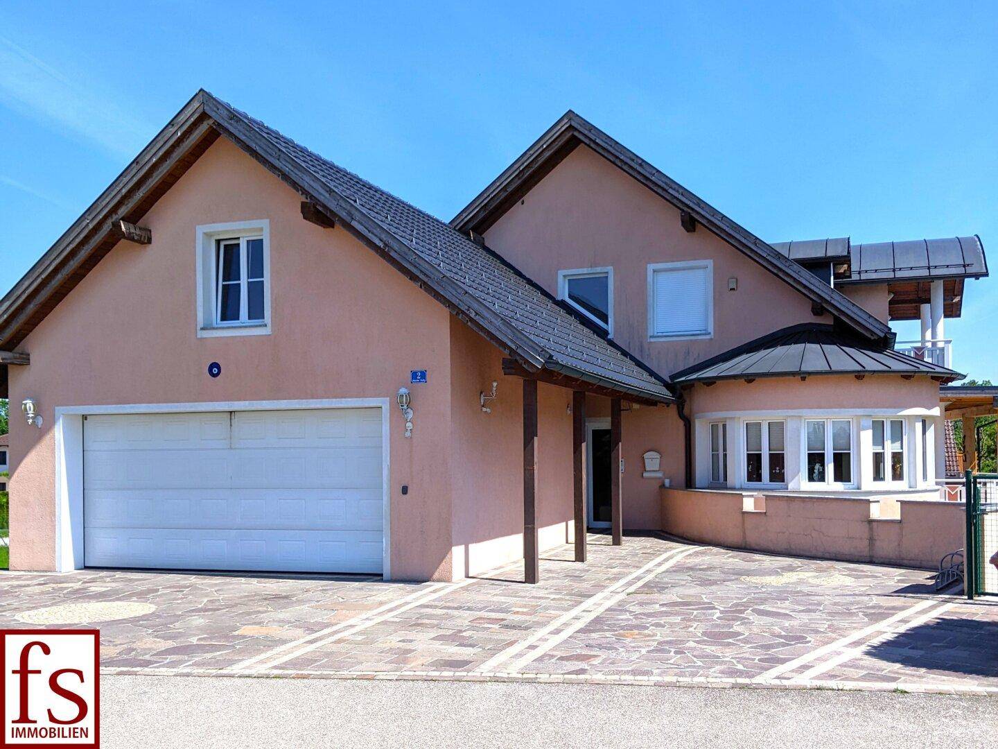 Vorderansicht des Hauses mit Doppelgarage, gepflasterter Auffahrt und Erkerfenster.