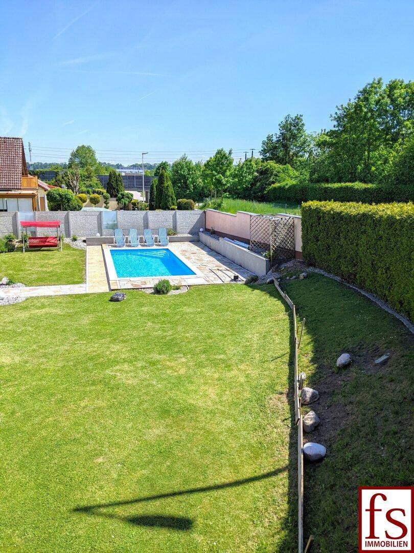 Weitläufiger Garten mit Rasenfläche, Pool und umgebender Hecke unter blauem Himmel.