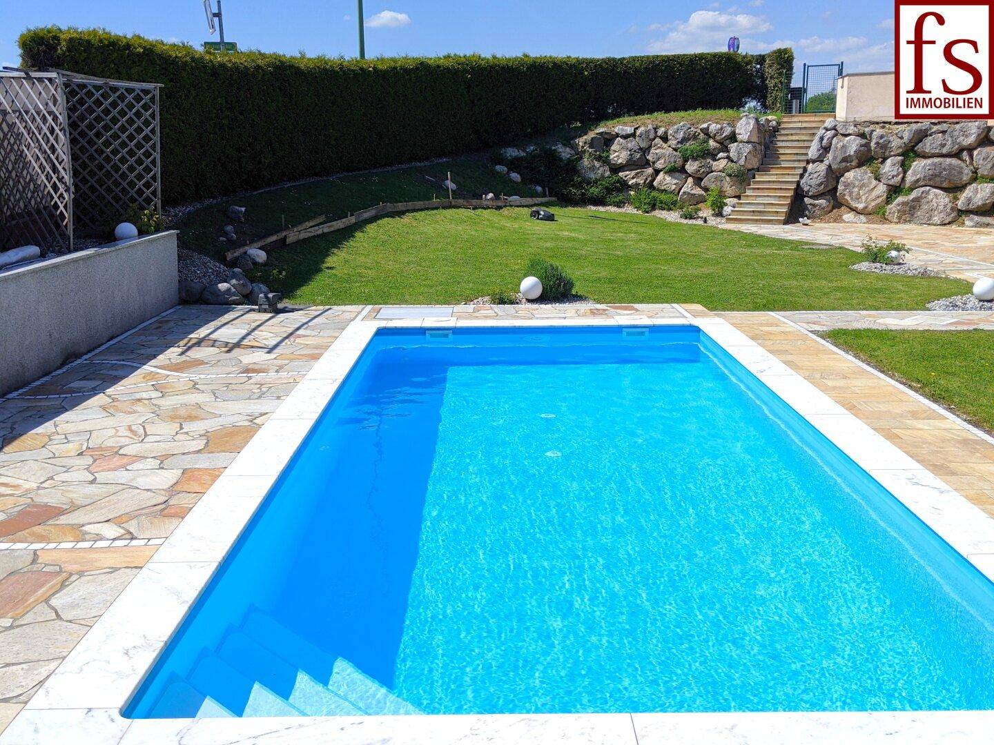 Nahaufnahme des Pools mit gefliestem Rand und gepflasterter Fläche, umgeben von Rasen.
