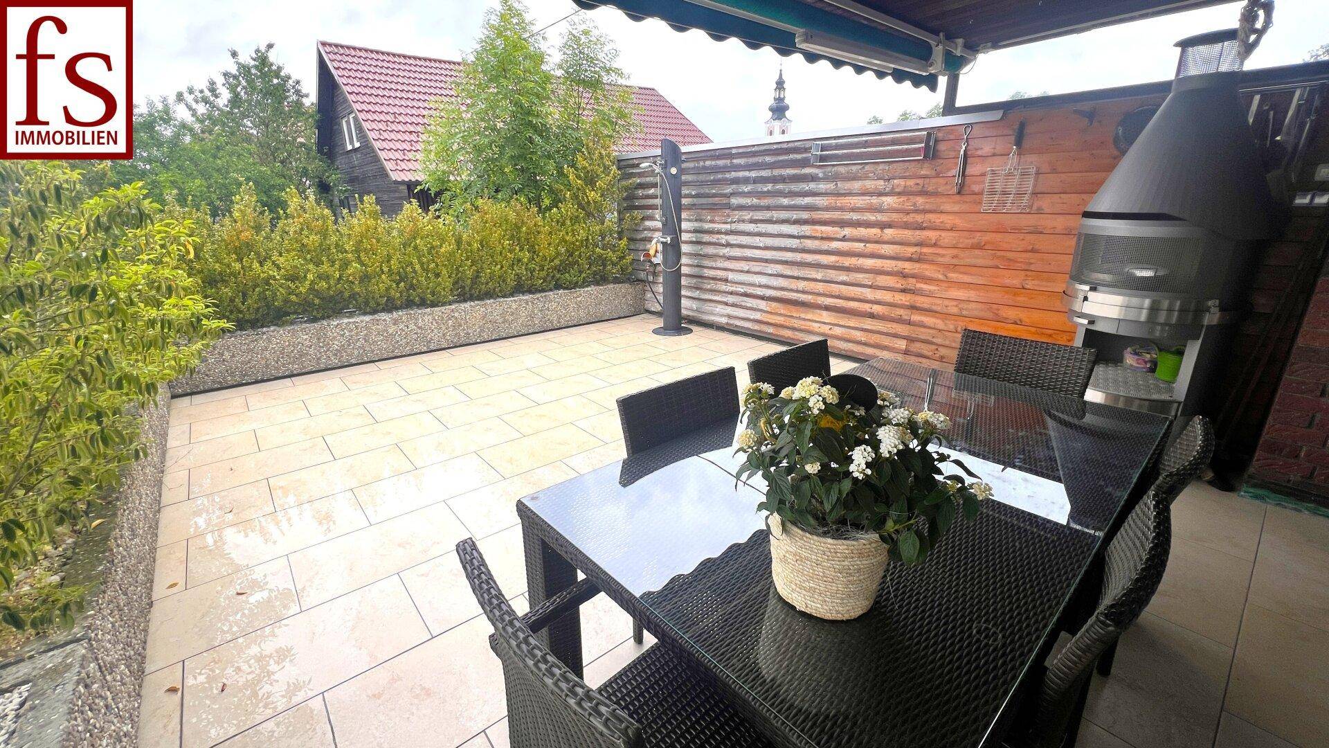 Große, geflieste Terrasse mit Esstisch, Grill und Sichtschutz.