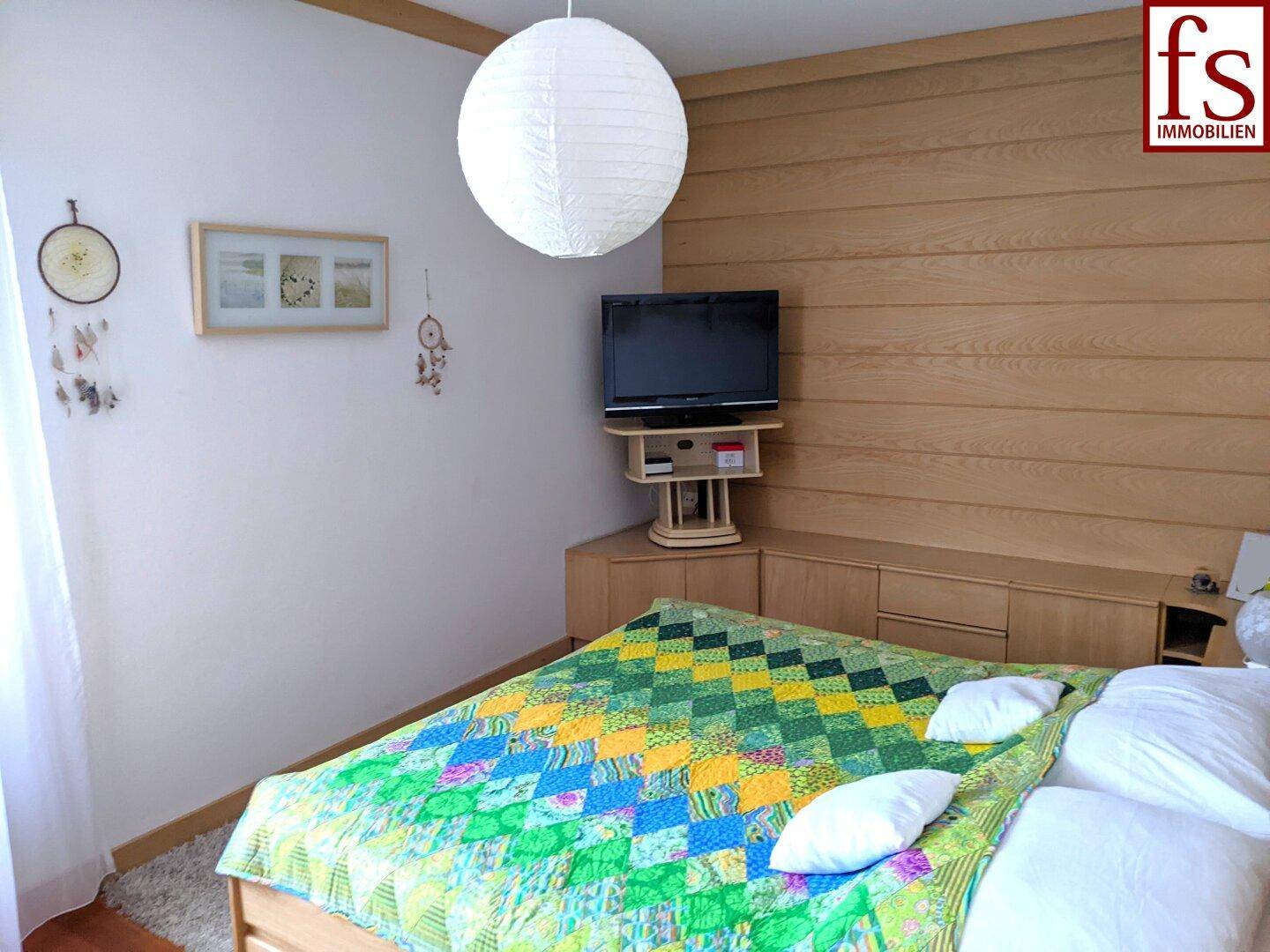 Gemütliches Schlafzimmer mit Holzwandverkleidung, Doppelbett und farbenfroher Bettdecke.