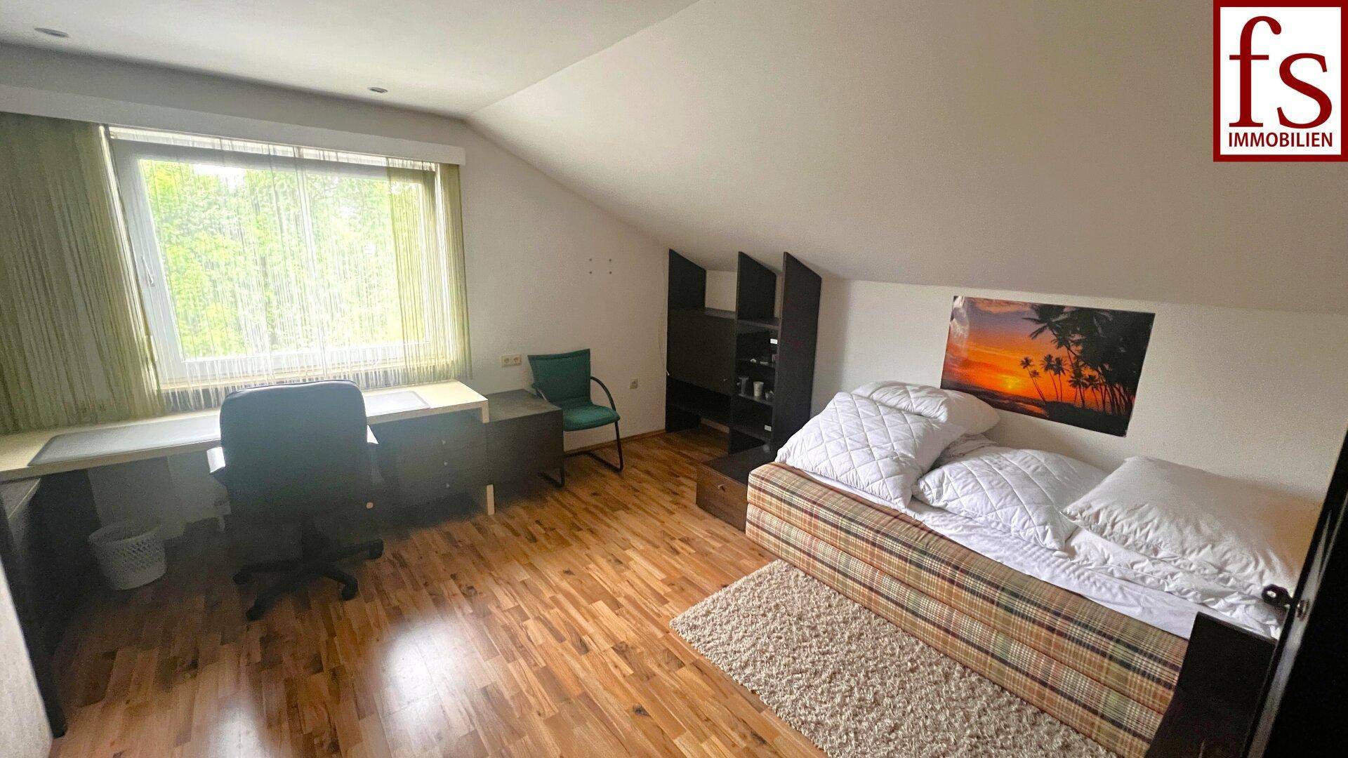 Helles Schlafzimmer im Dachgeschoss mit Schreibtisch, Bett und Holzboden.