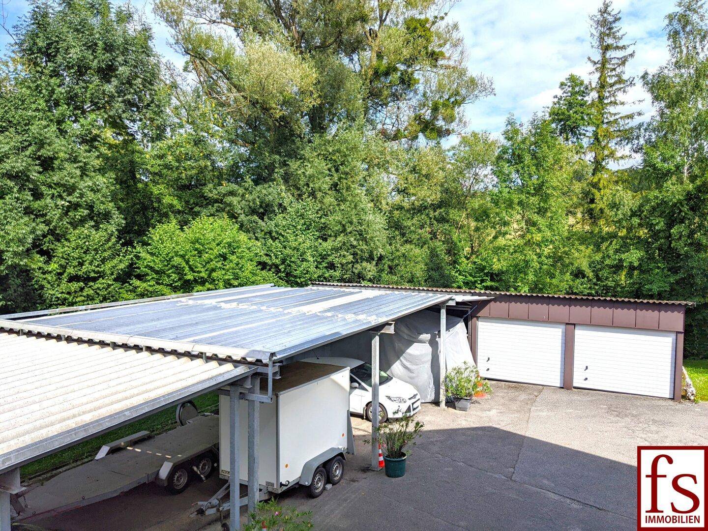 Überdachter Carport und Garagen mit viel Grün im Hintergrund.