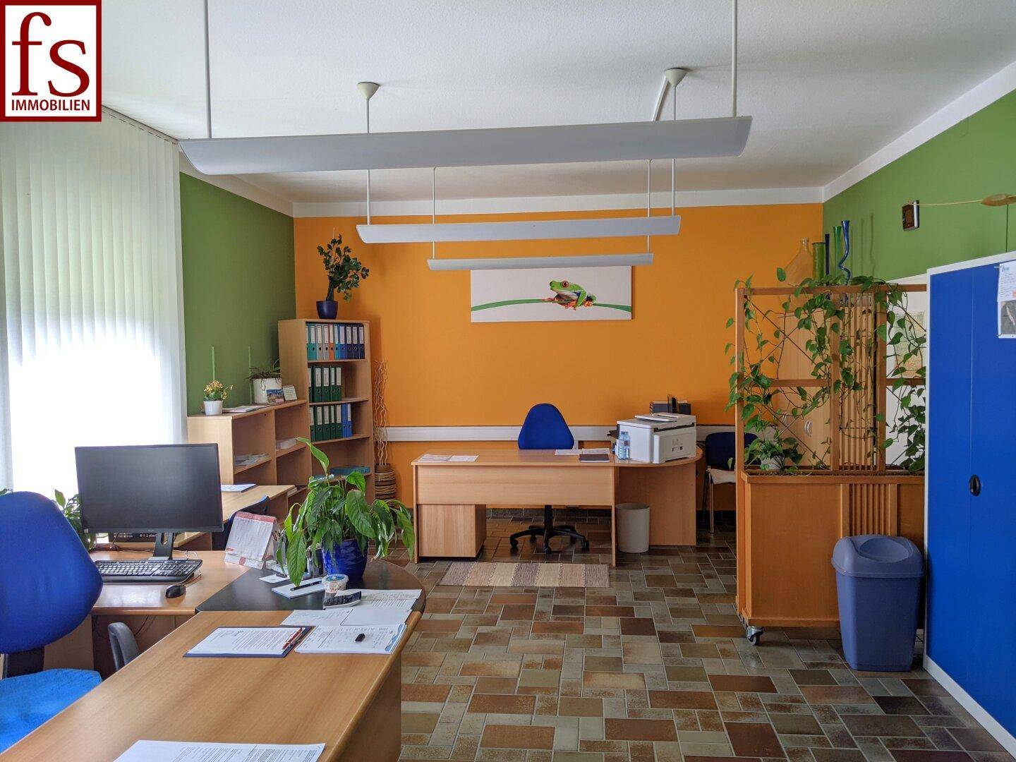 Helles Büro mit Schreibtischen, Regalen und freundlicher Farbgestaltung.
