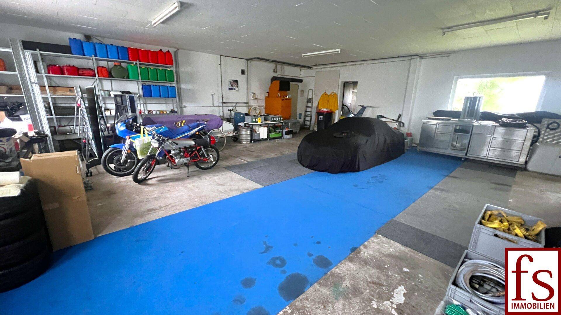 Geräumige Garage mit Werkstattbereich, Lagerregalen und Fahrzeugen.
