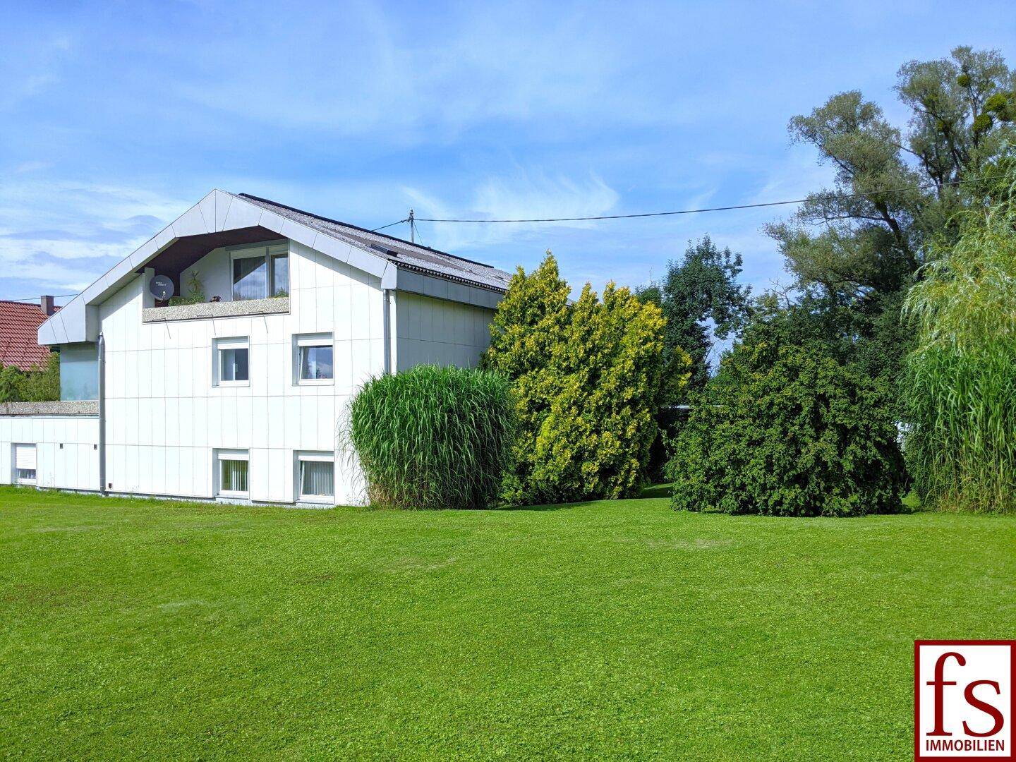Hausansicht mit großem, gepflegtem Rasen und üppiger Bepflanzung.