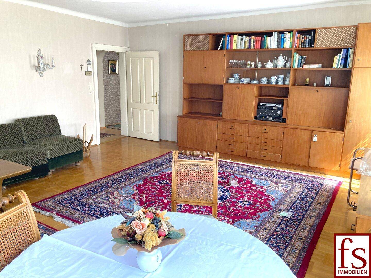 Wohnbereich mit Parkettboden, großem Teppich und einer umfangreichen Holzschrankwand.