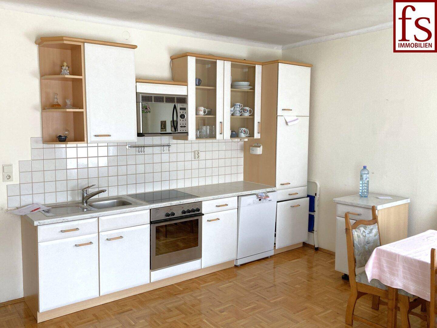 Helle Küche mit weißen Schränken, Fliesenrückwand und integrierten Elektrogeräten.