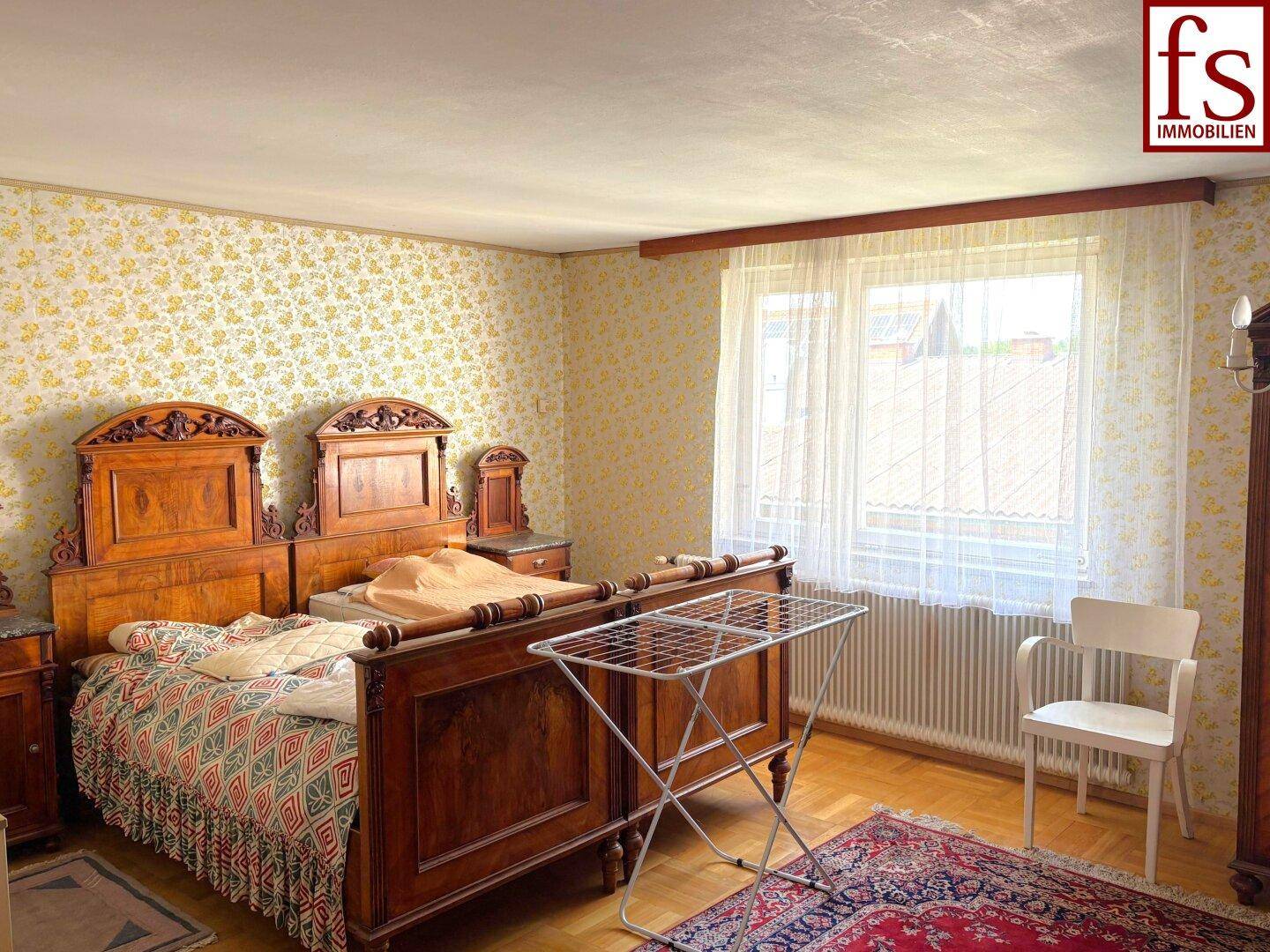 Schlafzimmer mit zwei traditionellen Holzbetten, gemusterter Tapete und Parkettboden.