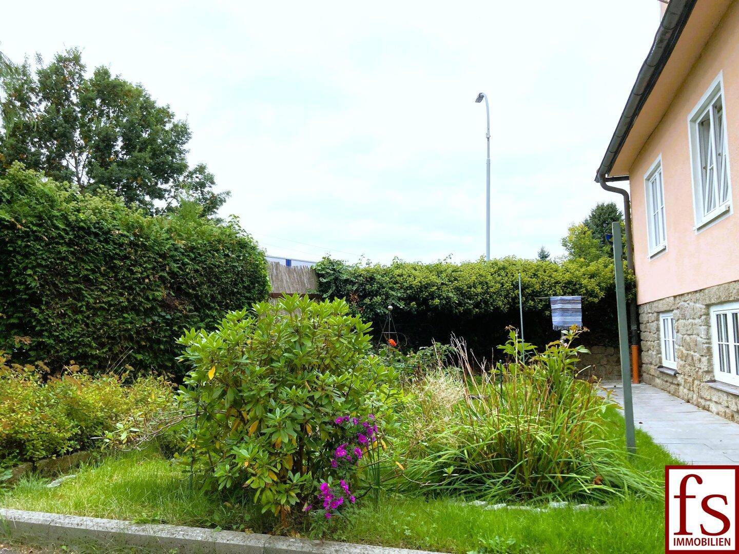 Gepflegter Gartenbereich mit Hecken, Sträuchern und Rasenfläche neben dem Haus.