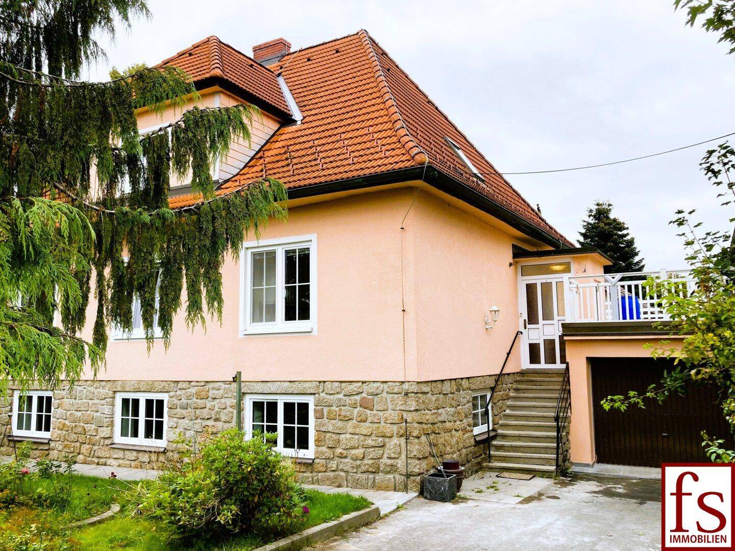Ansicht des Hauses mit Steinsockel, Ziegeldach und Zugang zu einem kleinen Balkon über eine Außentreppe.