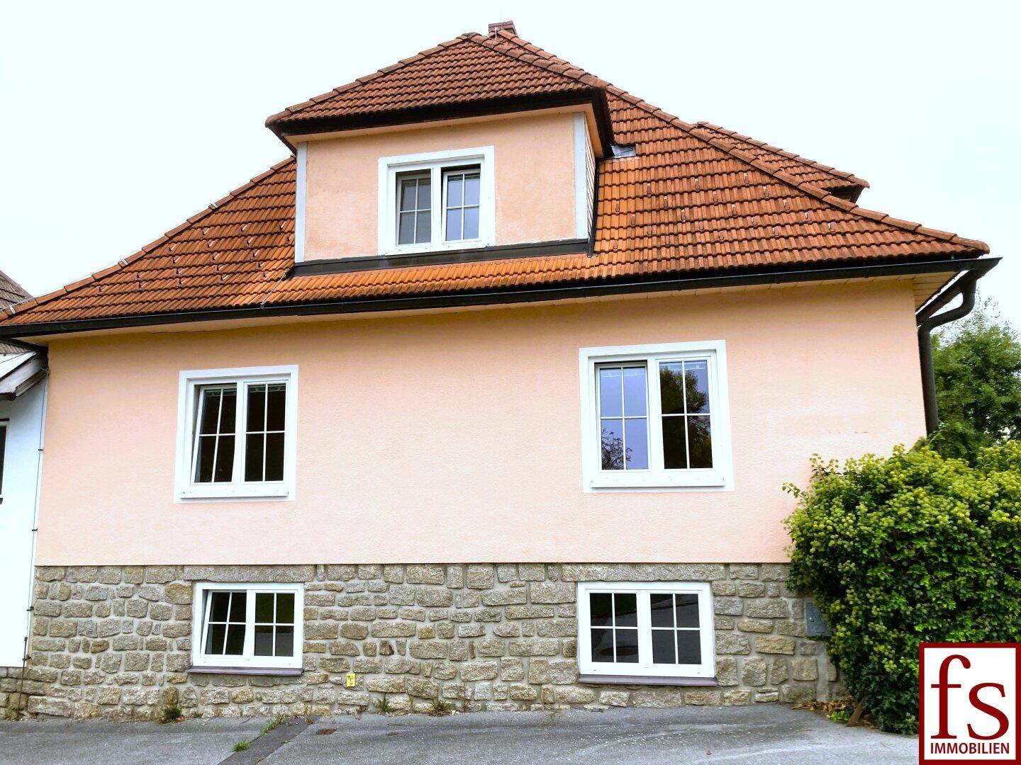 Vorderansicht des traditionellen Hauses mit Putzfassade, Steinsockel und Ziegeldach.